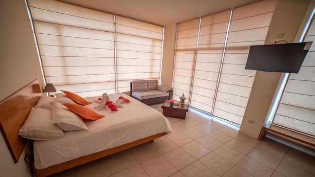 Quarto com uma cama, uma cadeira, uma mesinha e uma televisão.