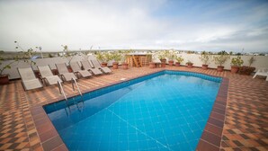 Piscina no terraço com piso de azulejos, espreguiçadeiras e plantas em vasos.