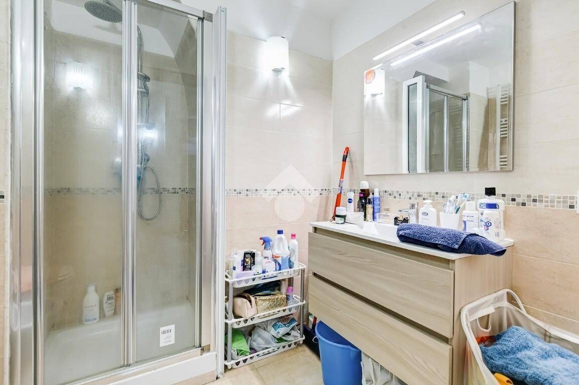 A modern bathroom with a glass shower enclosure, a vanity with toiletries, and a large mirror.