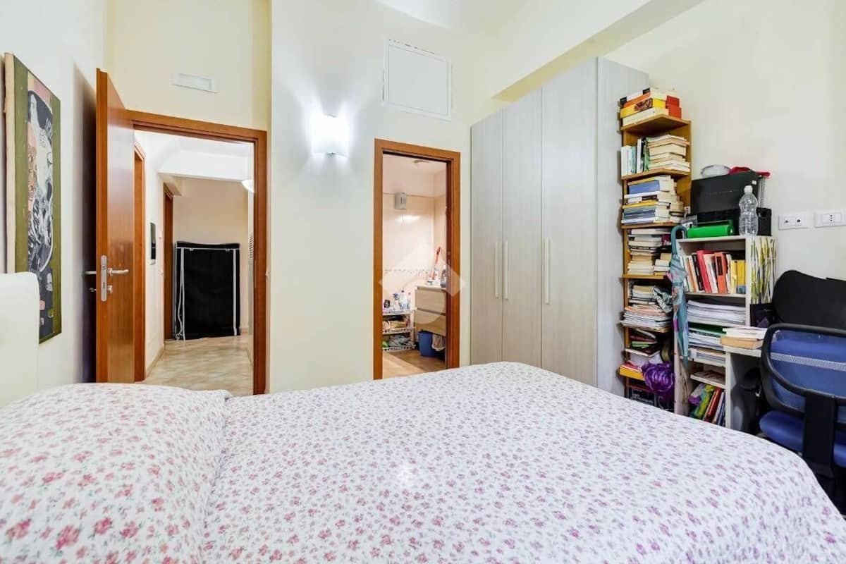 A bedroom with a bed, a wardrobe, a desk with a chair, and a bookshelf.