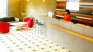 Zona de recepción de un hotel con diseño moderno, que incluye un mostrador, un área de estar con una silla roja y un suelo estampado.