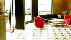 Un vestíbulo moderno con un sofá rojo, una mesa de centro blanca y un ventanal con vistas a la calle.