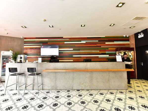 Mostrador de recepción con pantalla digital, taburetes de bar y suelo estampado.