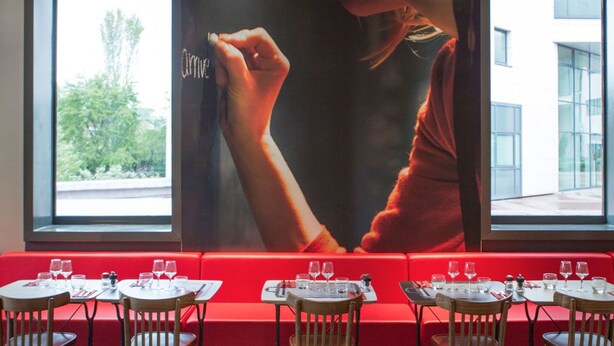 Un restaurante con asientos rojos, mesas con sillas y un cartel grande en la pared.