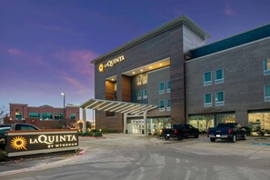 A La Quinta hotel with a modern design, featuring a prominent entrance and a parking area with several vehicles. - La Quinta Inn & Suites by Wyndham College Station South (College Station)