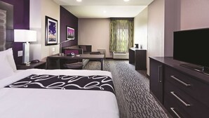 A hotel room with a bed, desk, chair, television, and a window with curtains.