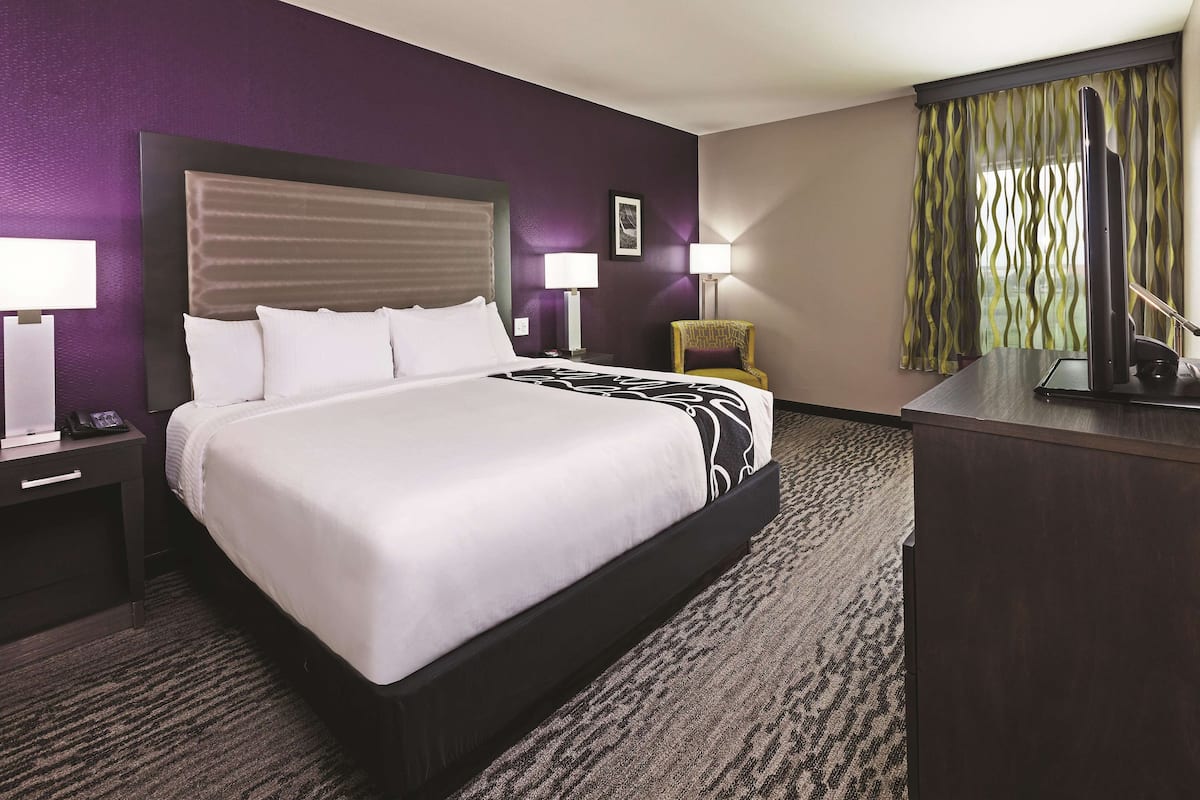 Habitación de hotel con una cama grande, dos mesitas de noche con lámparas, un escritorio con televisor y una silla.