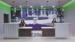 A reception desk with two attendants, a patterned wall, and a large digital display in the background.
