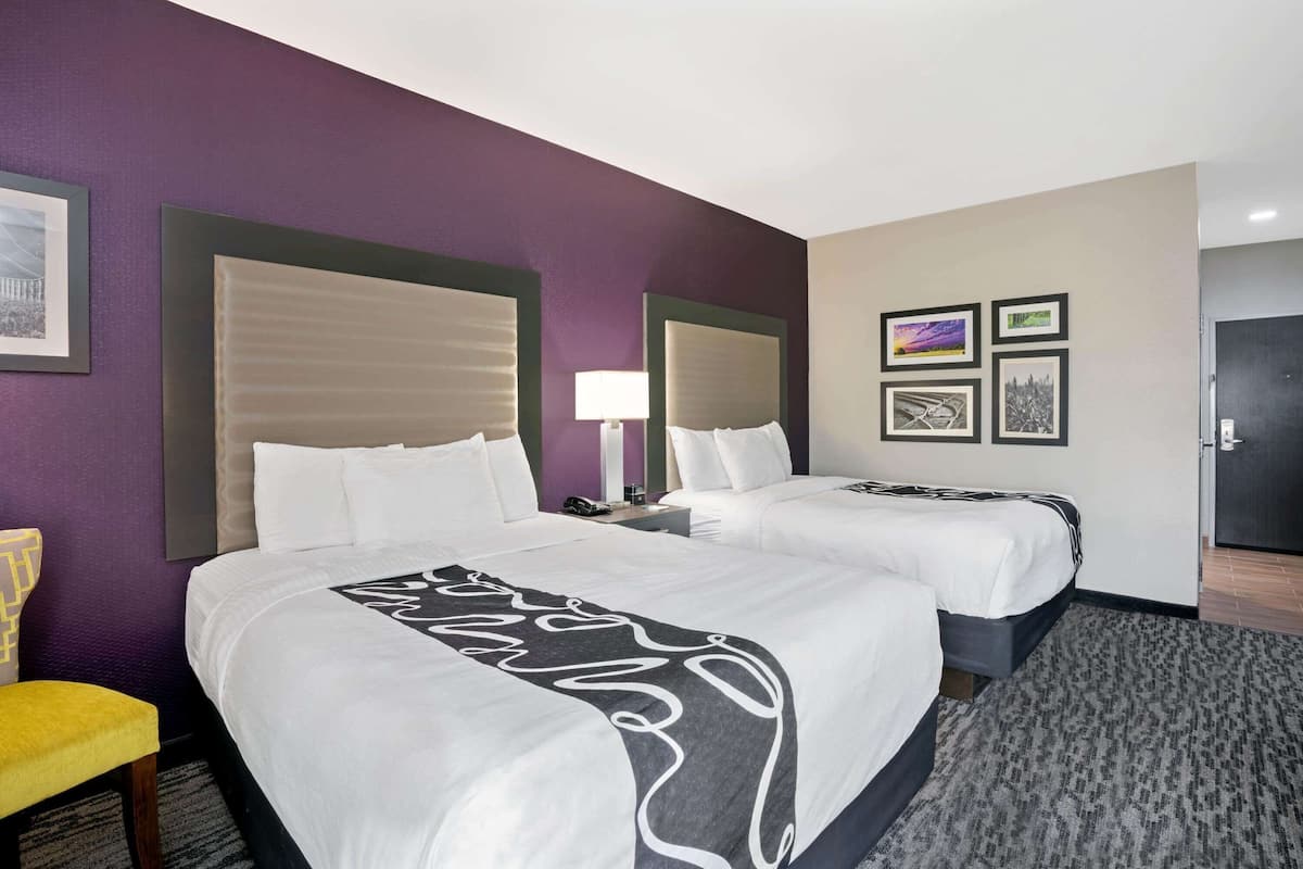 Habitación de hotel con dos camas, una silla, una lámpara y cuadros en la pared.