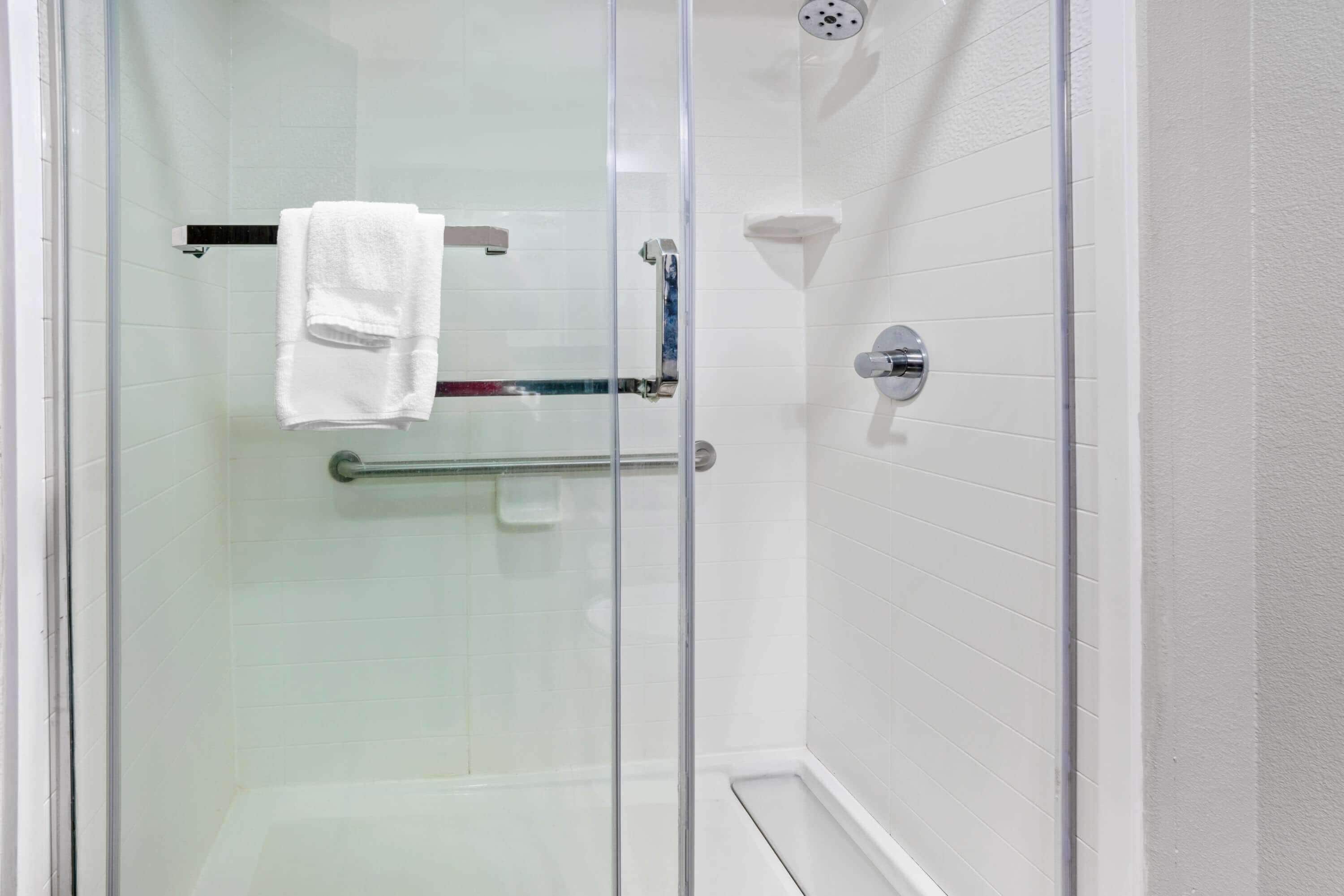 A glass-enclosed shower with a white tiled wall, a towel rack, and a glass shower door.