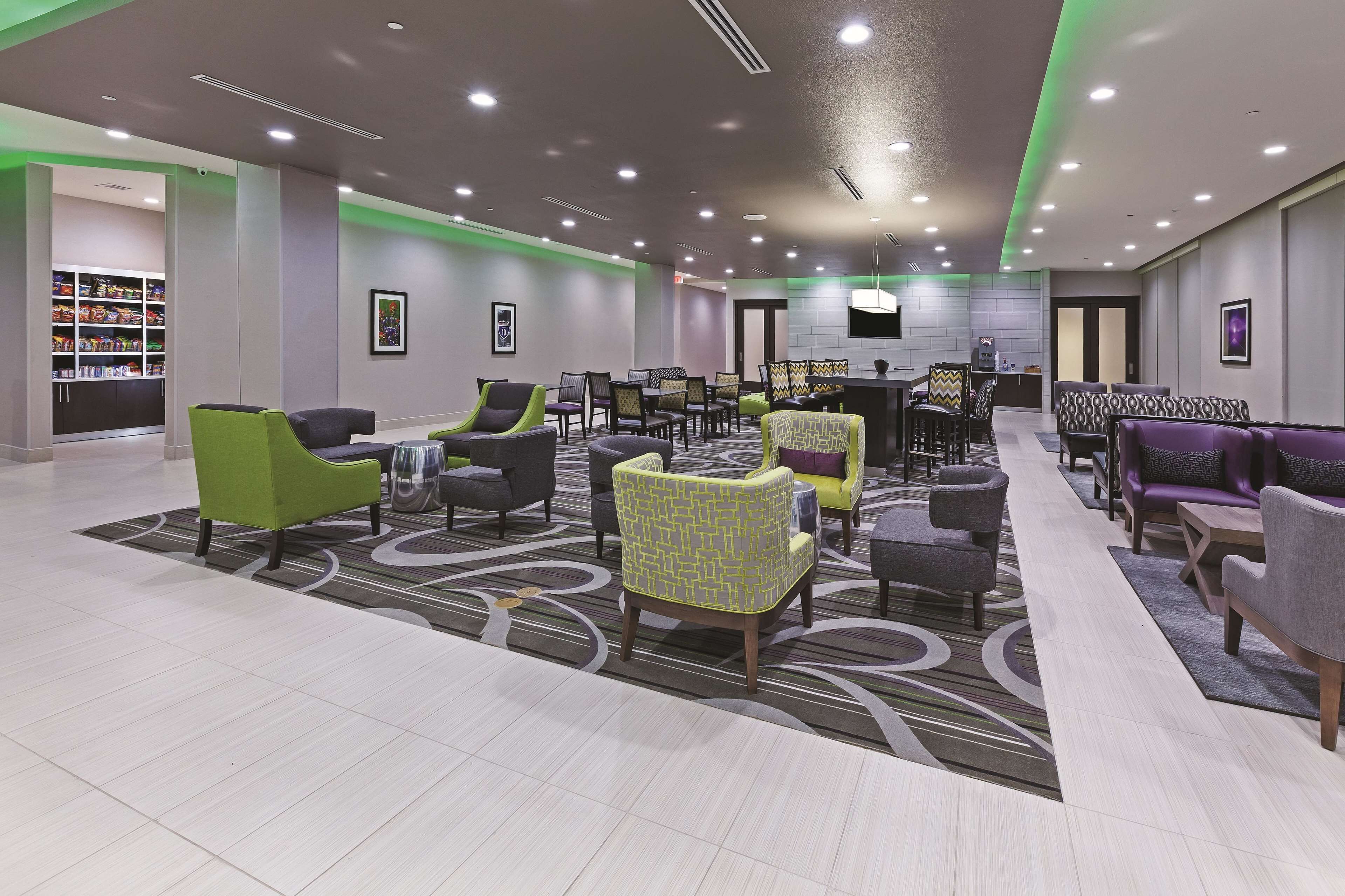 A modern lobby with seating areas, a reception desk, and a kitchen in the background.