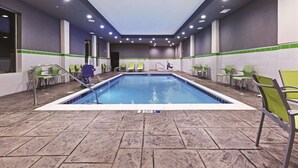 A swimming pool with chairs around it, a door in the background, and a tiled floor.