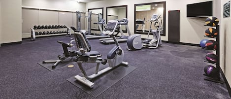 Un gimnasio con cintas de correr, máquinas de pesas y un estante con mancuernas.