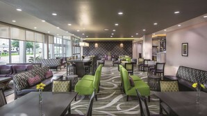 A modern hotel lobby with a mix of seating options, including sofas and chairs, arranged around a central area with a patterned carpet.