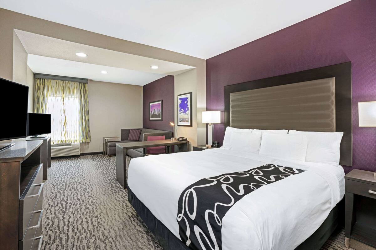 Habitación de hotel con una cama grande, un escritorio, una silla, un televisor y una ventana con cortinas.