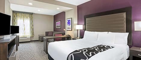 Habitación de hotel con una cama grande, un escritorio, una silla, un televisor y una ventana con cortinas.