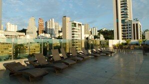 Espaço de lounge no terraço com espreguiçadeiras e vista para a cidade.