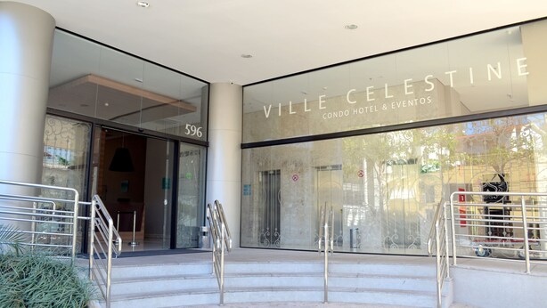 A entrada do Ville Celestine, um hotel com quartos tipo apartamento e espaço para eventos, com fachada de vidro e grades de metal.