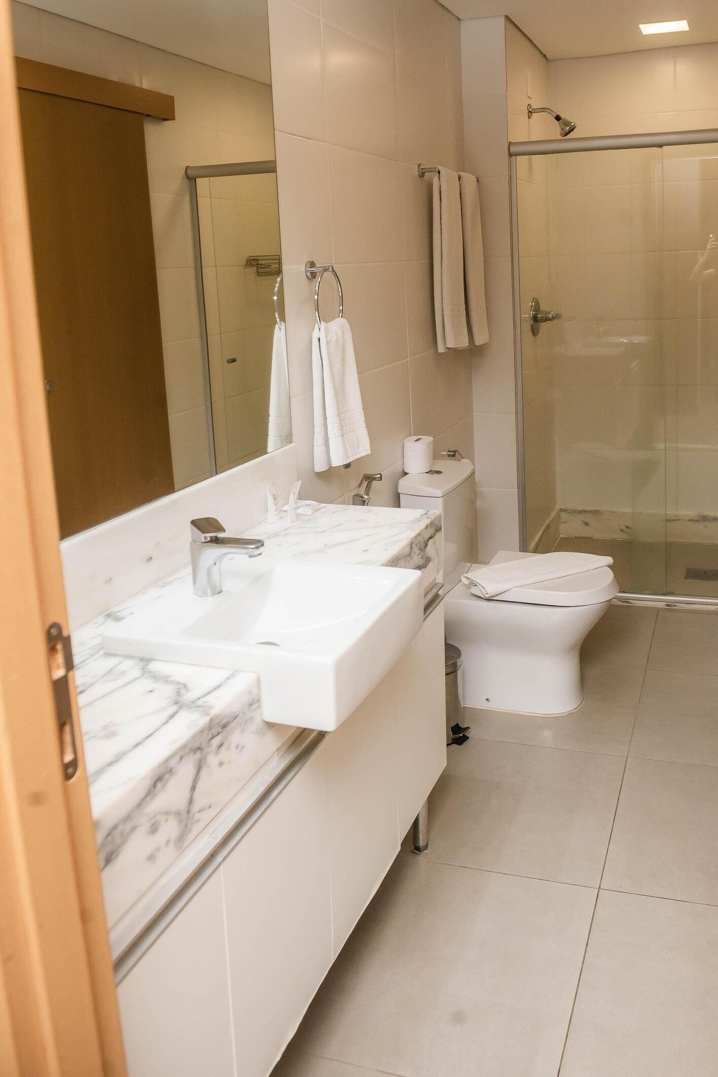 A modern bathroom with a marble countertop, a toilet, a shower, and a large mirror.