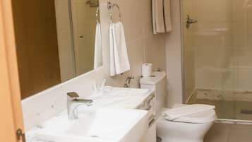 A modern bathroom with a marble countertop, a toilet, a shower, and a large mirror.