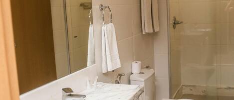 Un baño moderno con encimera de mármol, inodoro, ducha y un espejo grande.