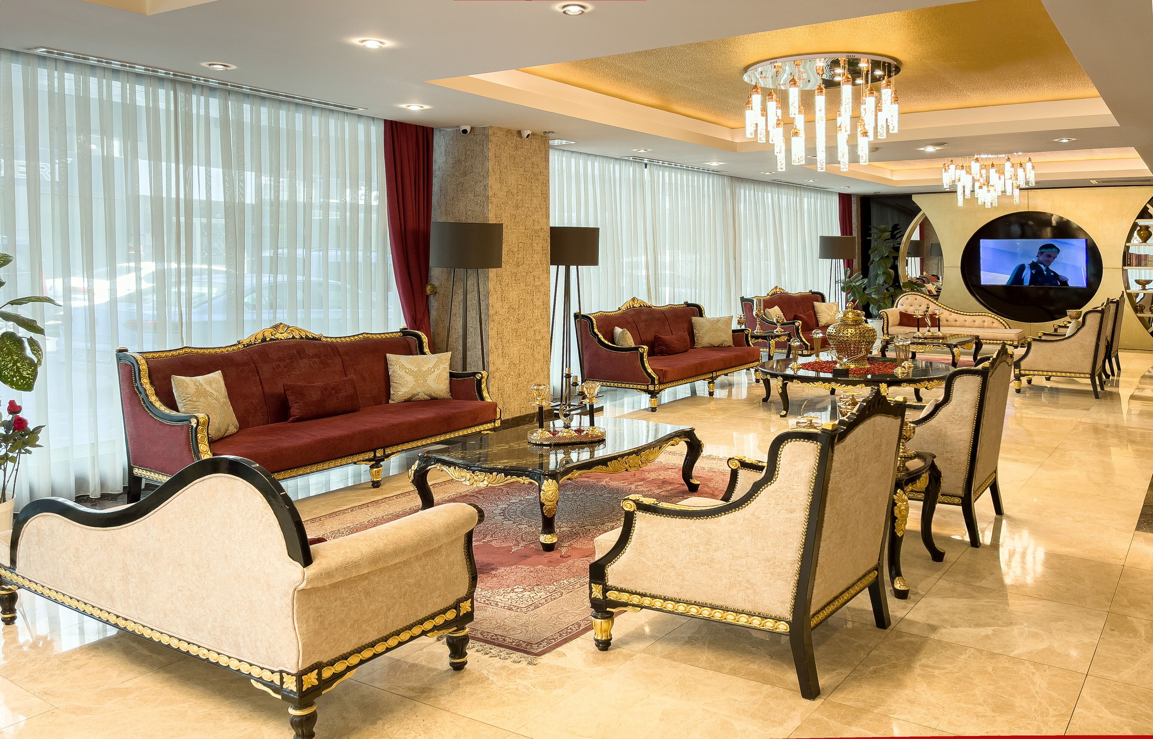 Ein luxuriöses Wohnzimmer mit einem roten Sofa, beigen Sesseln, einem Glastisch und einer Kristallleuchter.