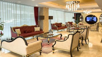 Ein luxuriöses Wohnzimmer mit einem roten Sofa, beigen Sesseln, einem Glastisch und einer Kristallleuchter.