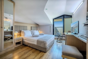 Una habitación de hotel moderna con una cama grande, un escritorio con ordenador, una silla y un televisor.