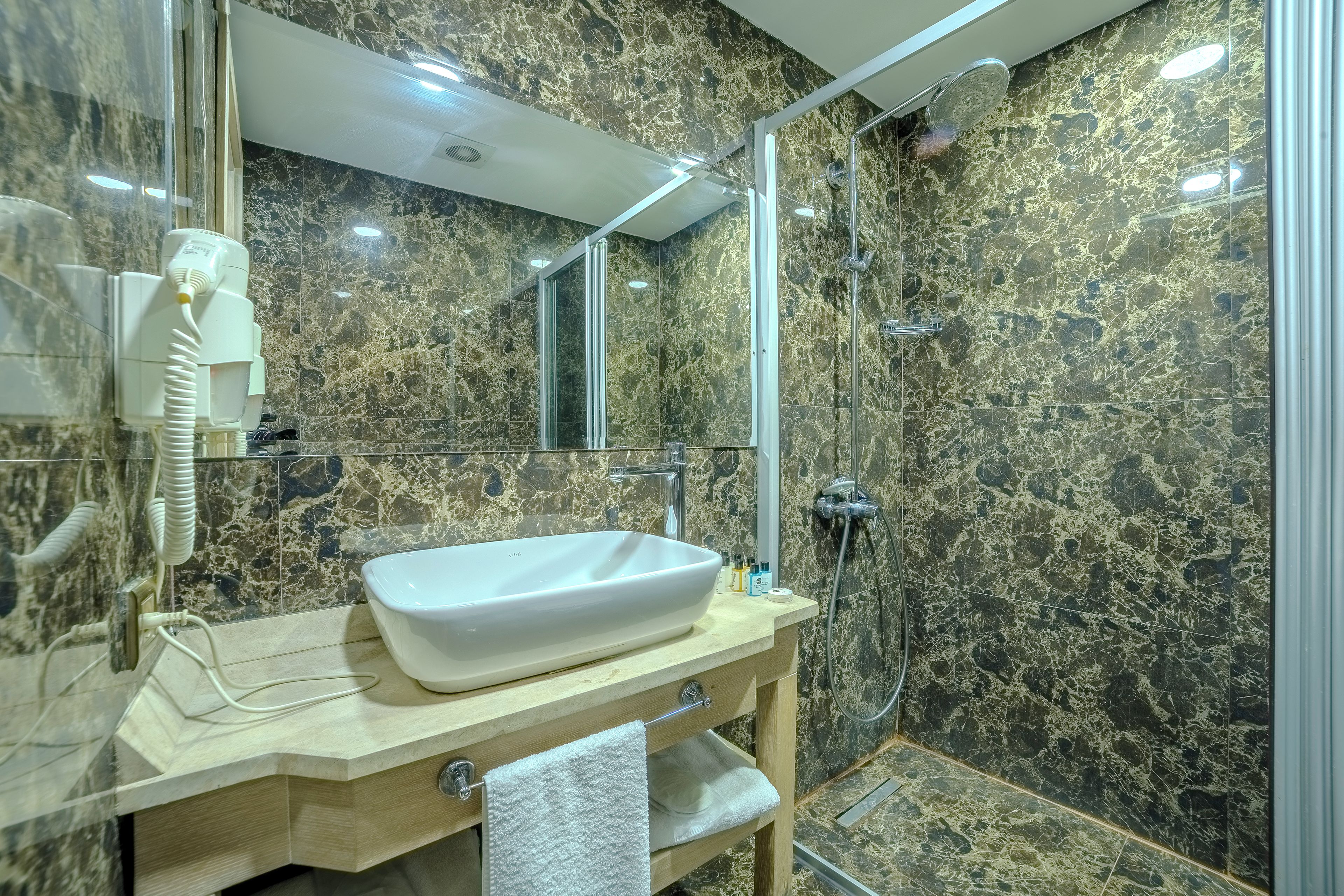 Une salle de bain avec un mur en marbre, un lavabo blanc et une cabine de douche en verre.