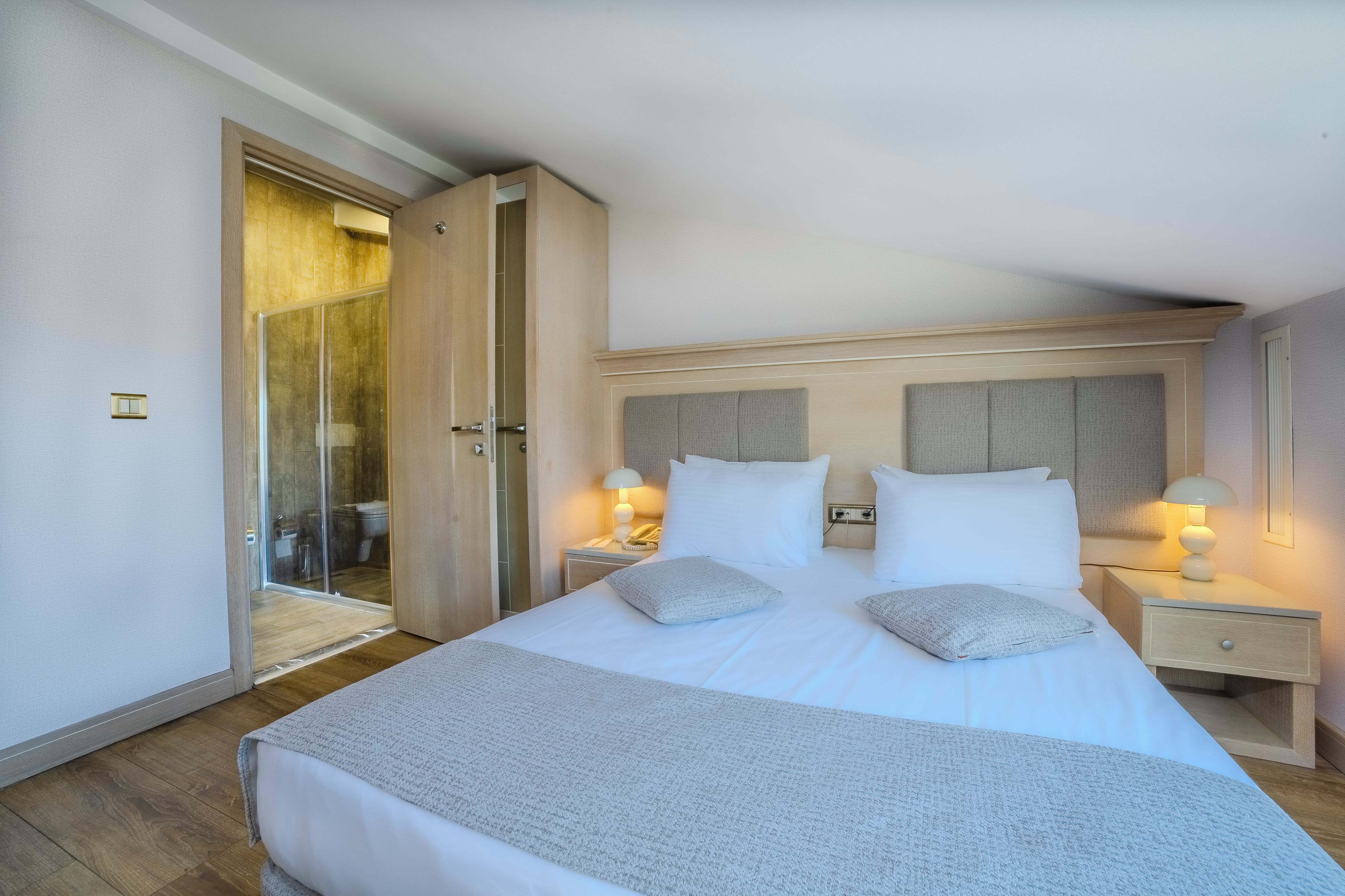 Une chambre d’hôtel avec un grand lit, des tables de chevet, une petite table, une lampe et une salle de bain visible à travers une porte ouverte.