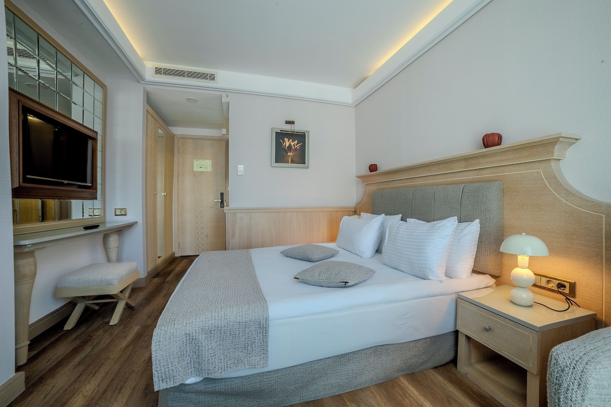 A neatly arranged bedroom with a bed, bedside table, lamp, and a television mounted on the wall.