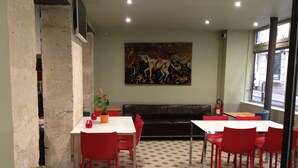 A dining area with red chairs and tables, a black leather couch, and a large abstract painting on the wall. - Hôtel du Jura (Paris)