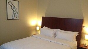 A neatly made bed with white linens, a wooden headboard, and two bedside lamps. - Hôtel du Jura (Paris)