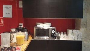 A breakfast area with a microwave, coffee maker, and stacked cups. - Hôtel du Jura (Paris)