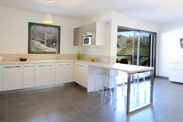 A modern kitchen with white cabinets, a built-in microwave, and a large window. - Les Terrasses Du Grand Large (Serra-di-Ferro)