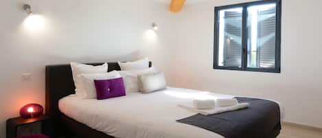 A neatly made bed with white and dark bedding, a purple pillow, and a bedside lamp.