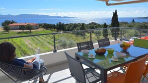 En balkon med et bord dækket til morgenmad, med udsigt over et smukt hav- og bjerglandskab.