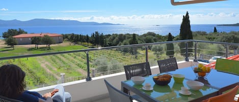 Un balcón con una mesa dispuesta para el desayuno, con vistas panorámicas al mar y a las montañas.