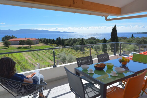 Un balcón con una mesa dispuesta para el desayuno, con vistas panorámicas al mar y a las montañas.