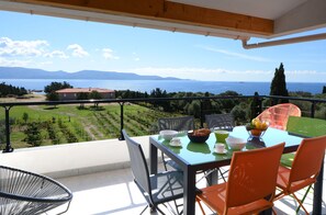 Ein Balkon mit Tisch für zwei Personen, Stühlen und Blick auf Meer und Berge.
