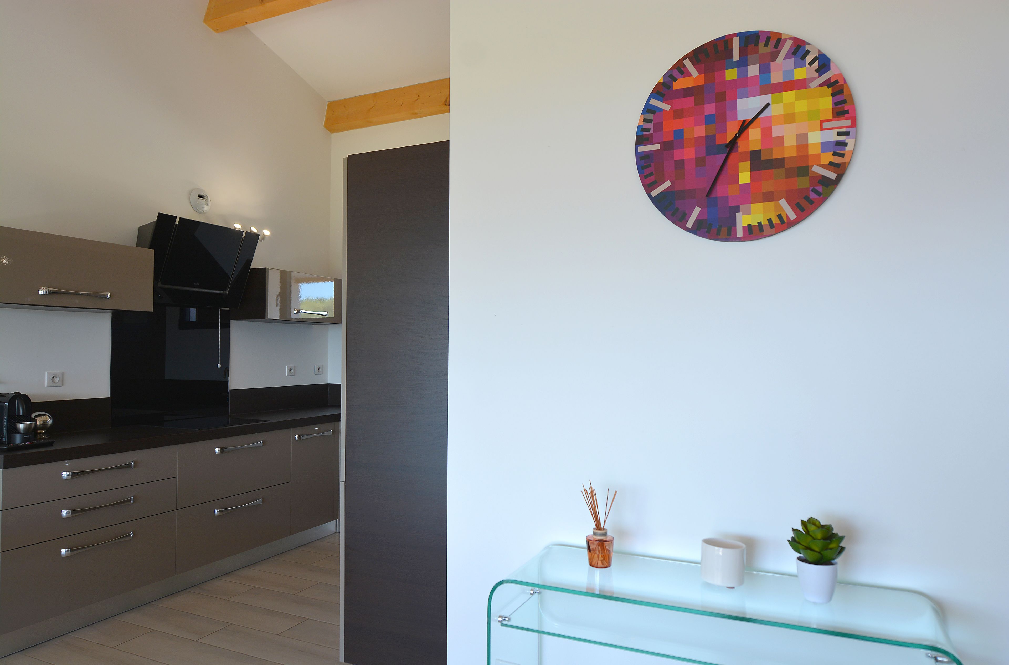 A modern kitchen with a dark countertop, a glass coffee table, a colorful clock, and a small plant.
