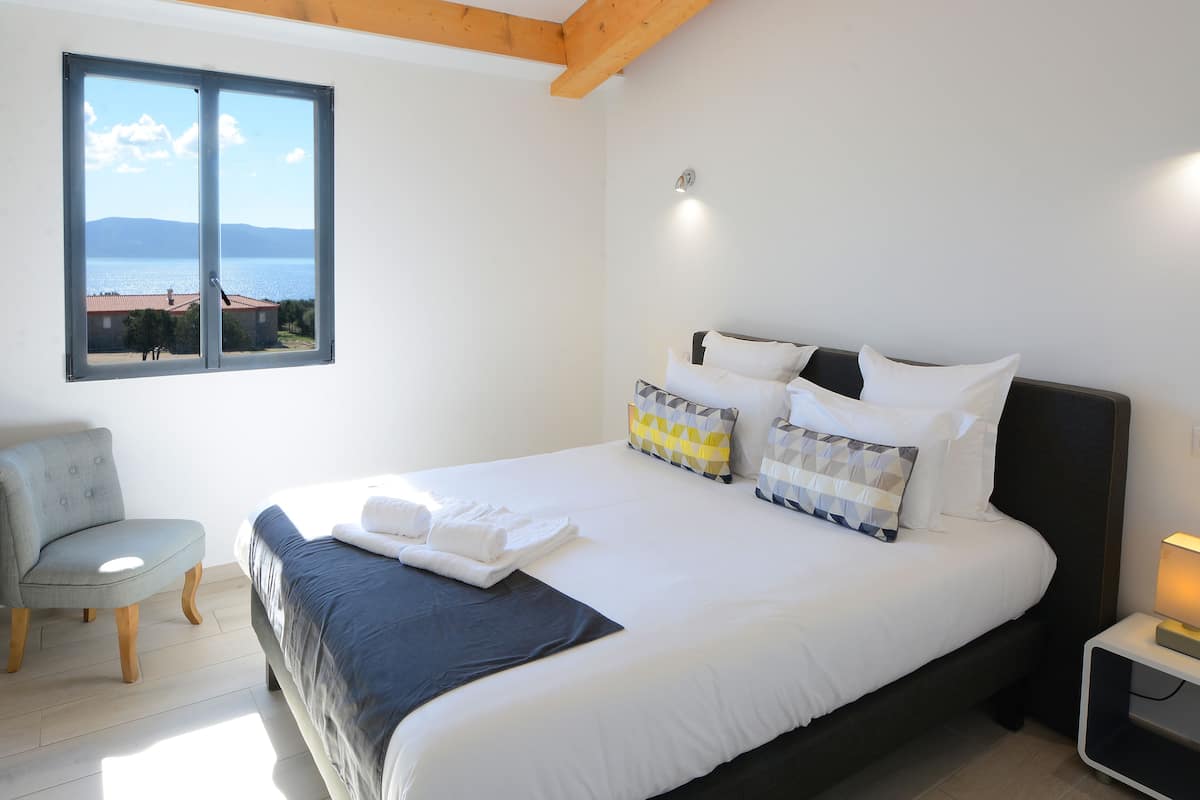 Un dormitorio con una cama, una silla, una mesita de noche y una ventana con vista al mar.