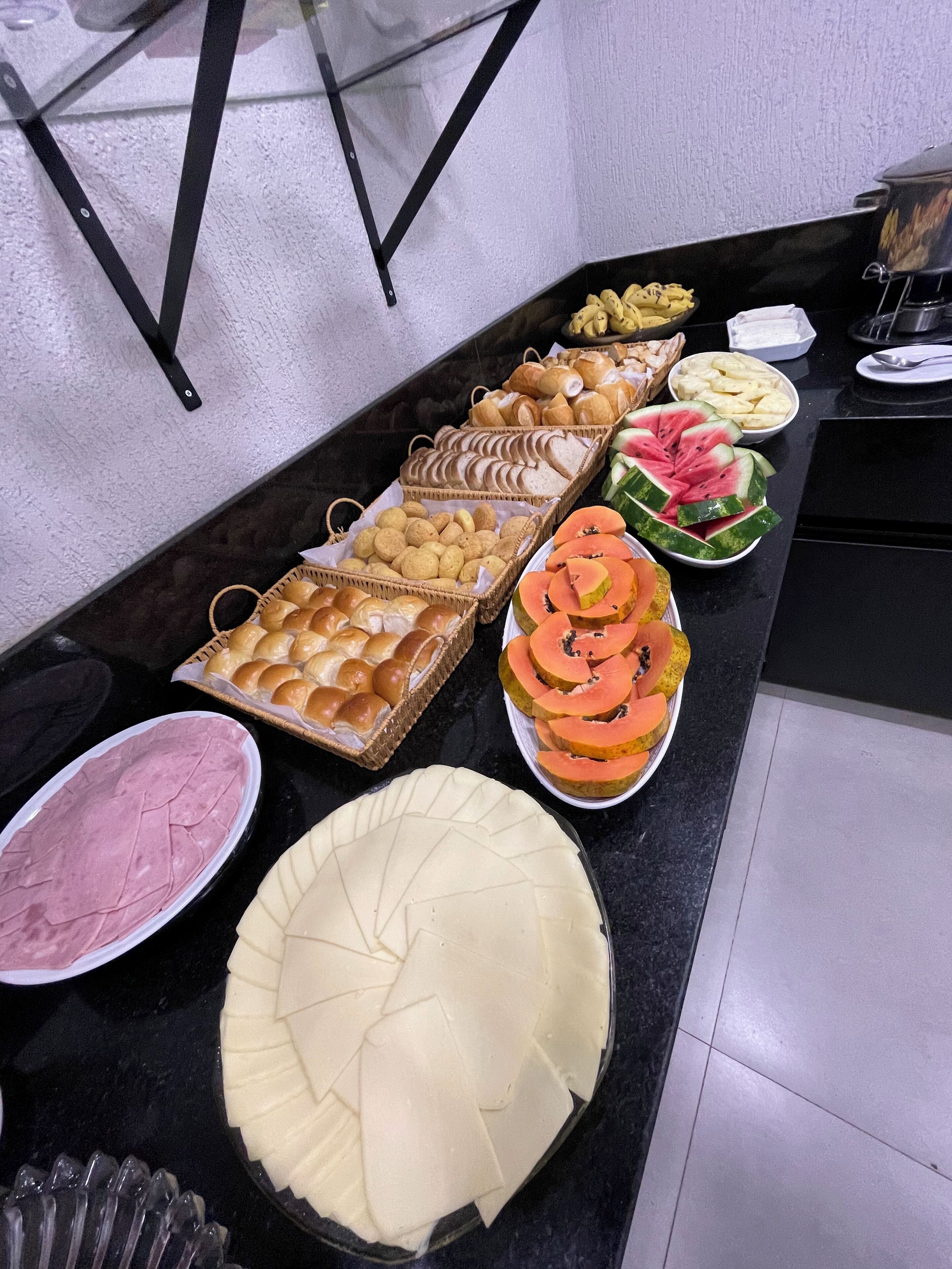 Una mesa de bufé con diferentes alimentos, como pan, pasteles y frutas cortadas.