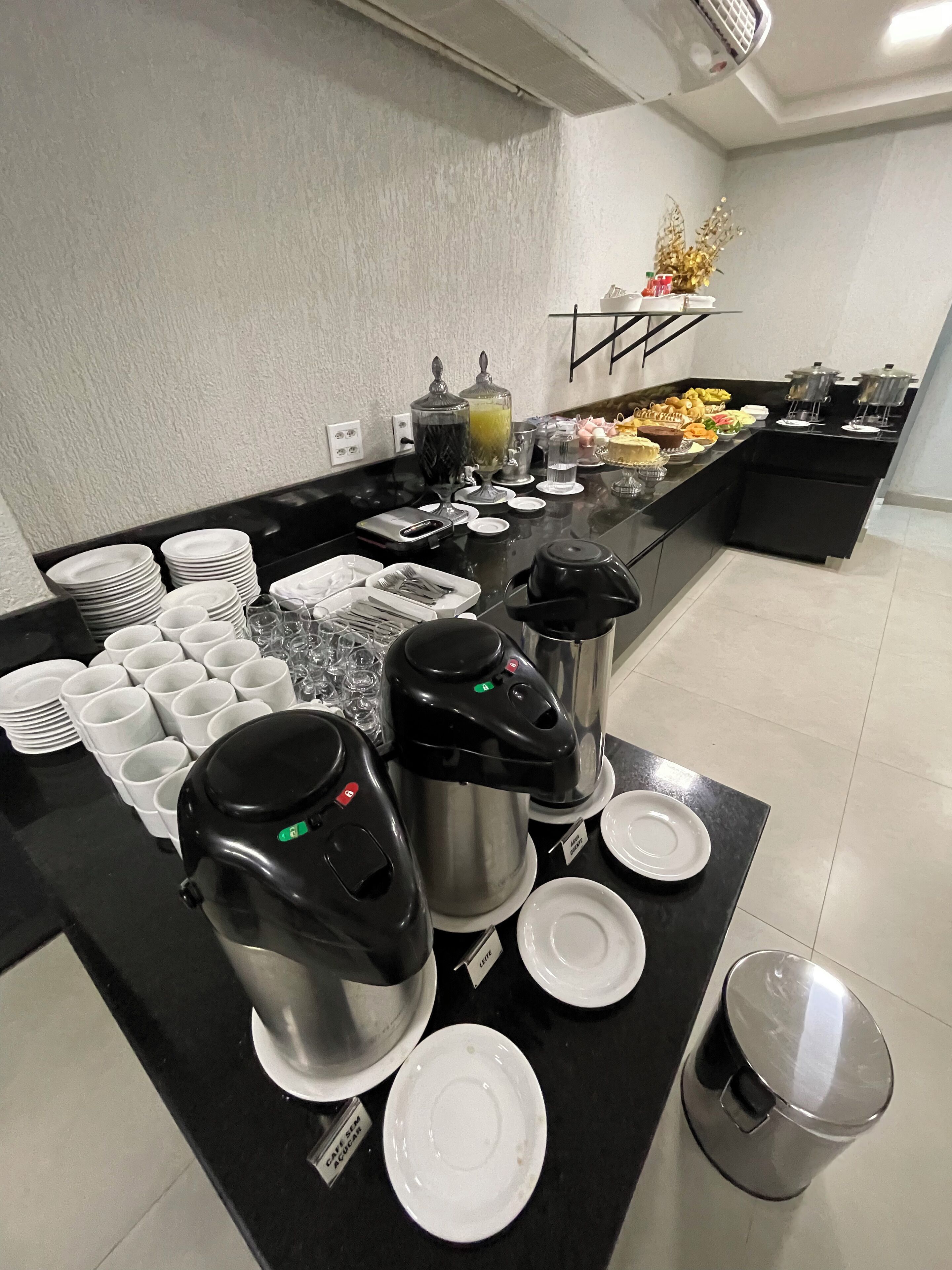 A buffet setup with coffee makers, plates, cups, and food items.