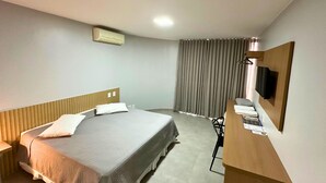 Habitación de hotel con cama, escritorio con silla, televisión de pantalla plana y ventana con cortinas.