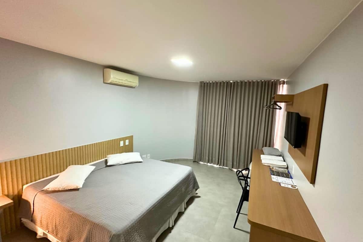 Habitación de hotel con cama, escritorio con silla, televisión de pantalla plana y ventana con cortinas.