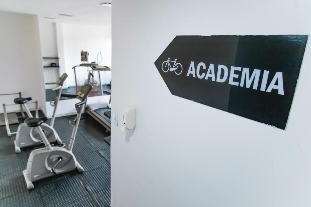 Um sinal com um símbolo de bicicleta e a palavra 'ACADEMIA' em uma parede branca.