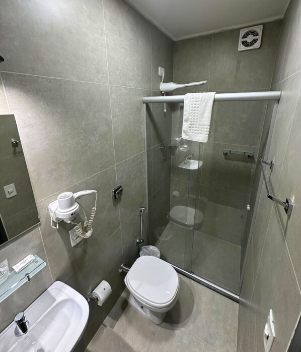 Un baño moderno con ducha envuelta en vidrio, inodoro, lavabo y toallero.