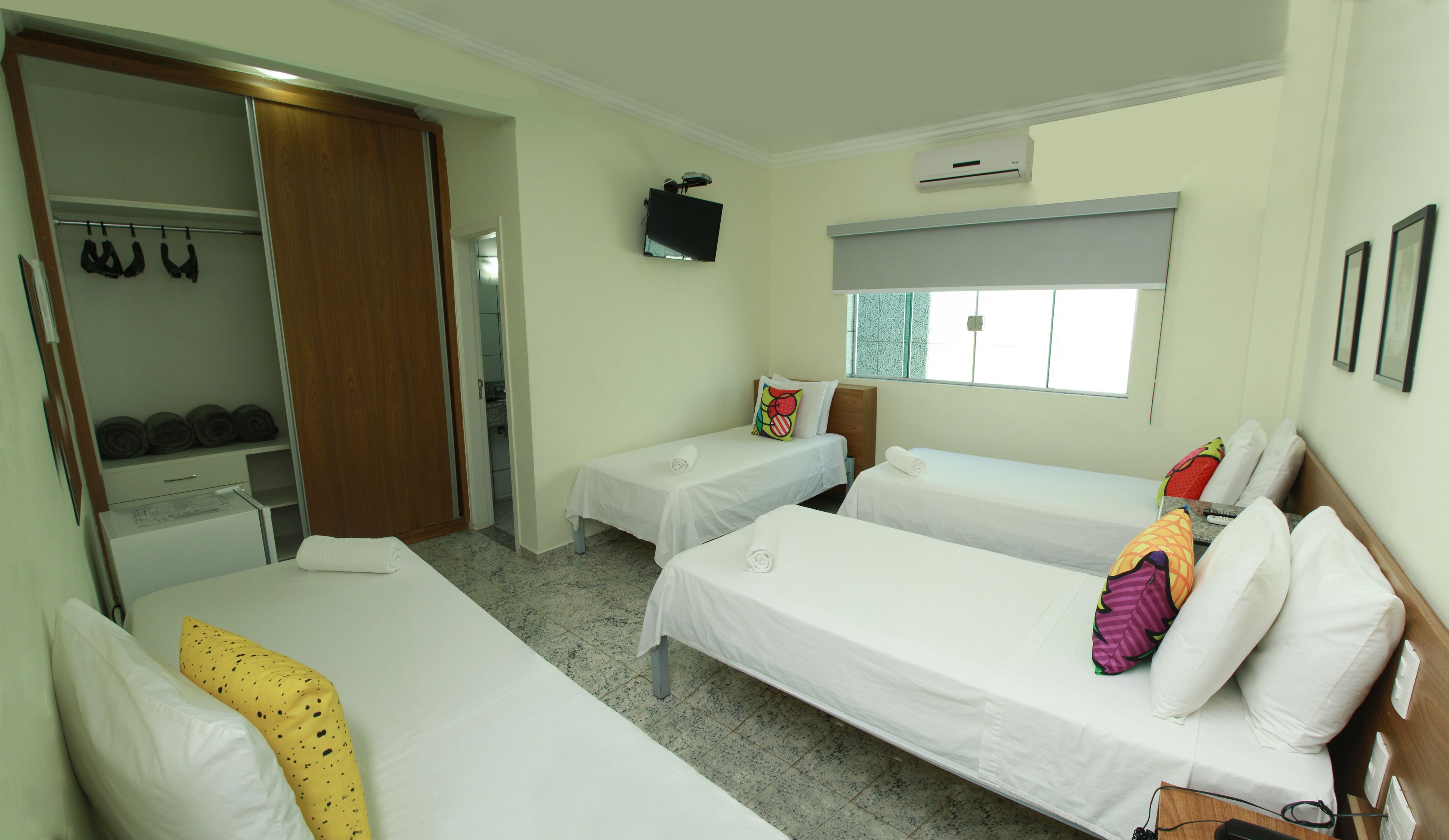 A hotel room with two single beds, a wardrobe, a television, and a window.