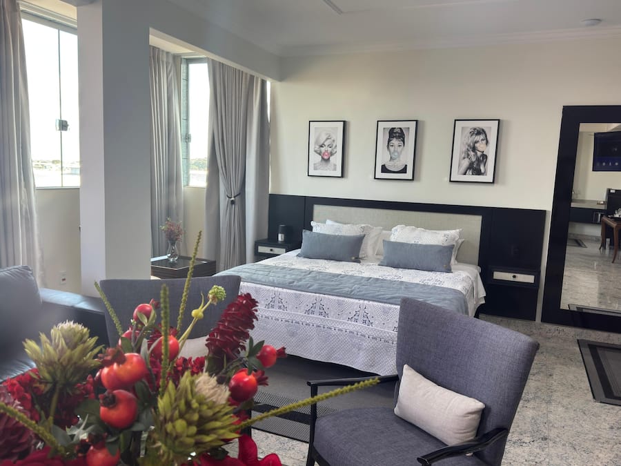 A hotel room with a bed, a chair, a nightstand, a bedside table, and a mirror.